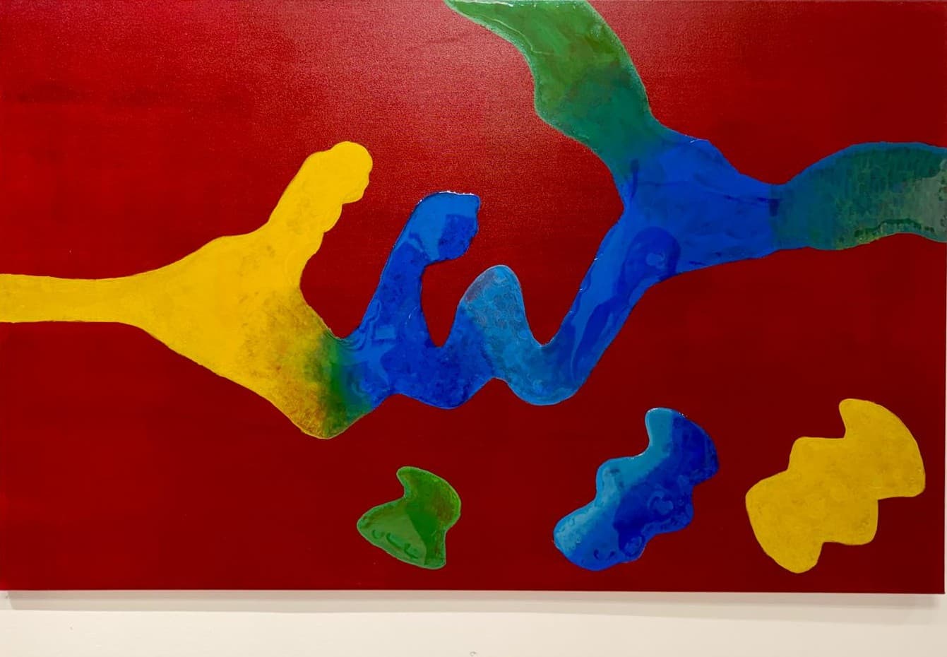 Abstract painting with yellow, blue and green organic forms meeting on a deep red ground