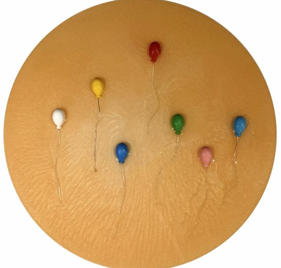 Round ochre panel with seven multicolored balloons, a red one rising highest