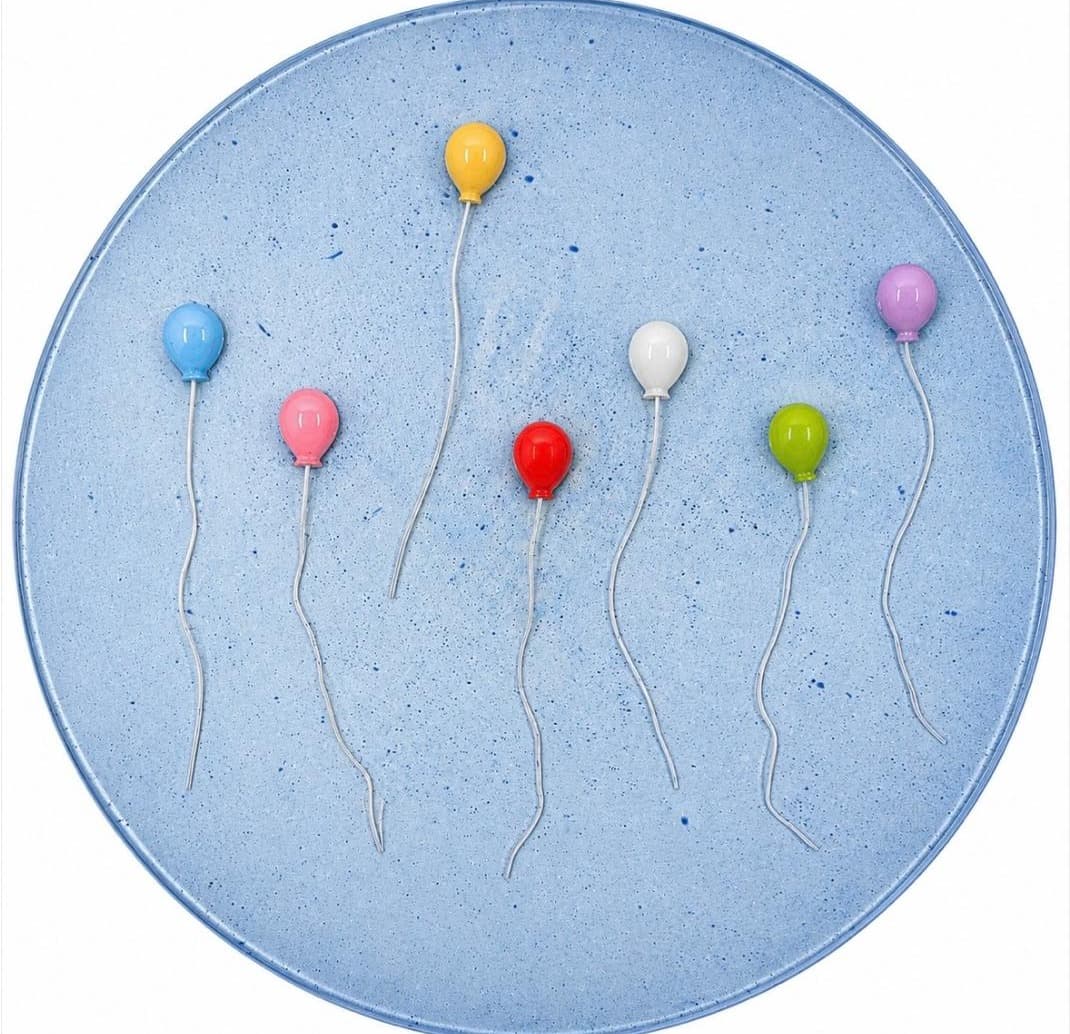 Round light blue speckled panel with seven balloons in primary and pastel colors