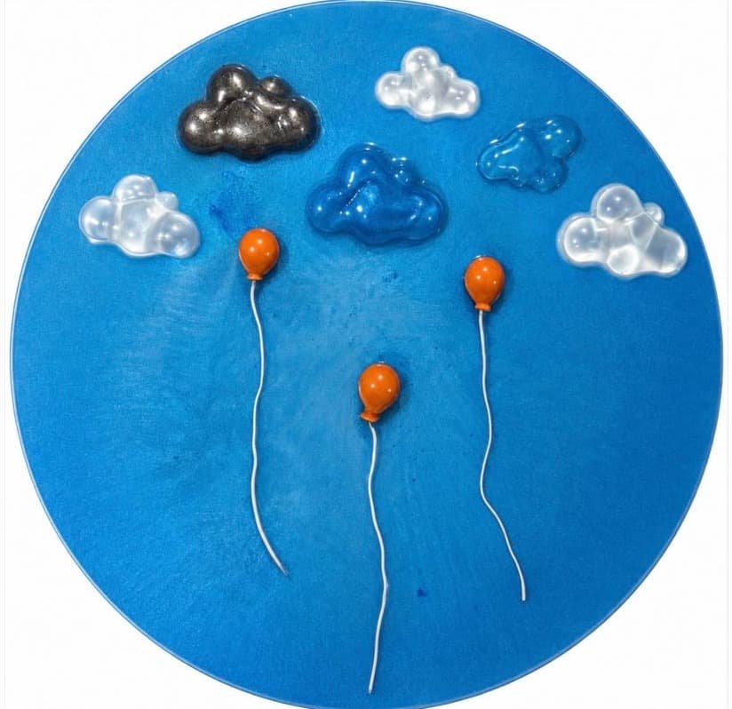 Round blue panel with three orange balloons under sculptural glass clouds