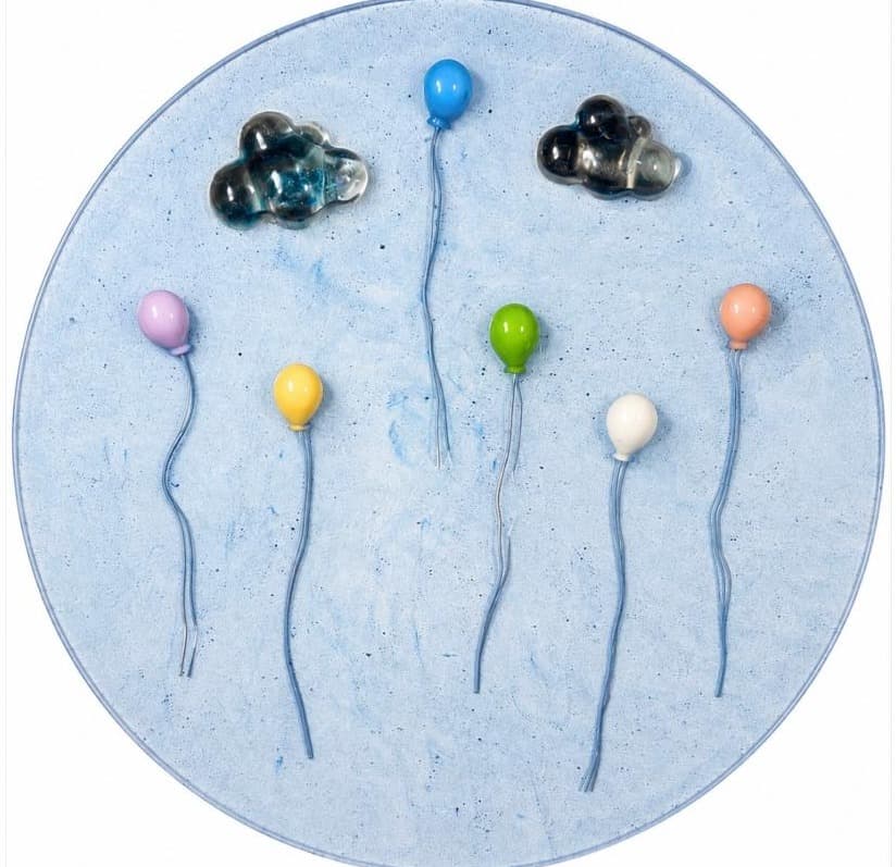 Round pale blue panel with dark glass clouds and pastel balloons