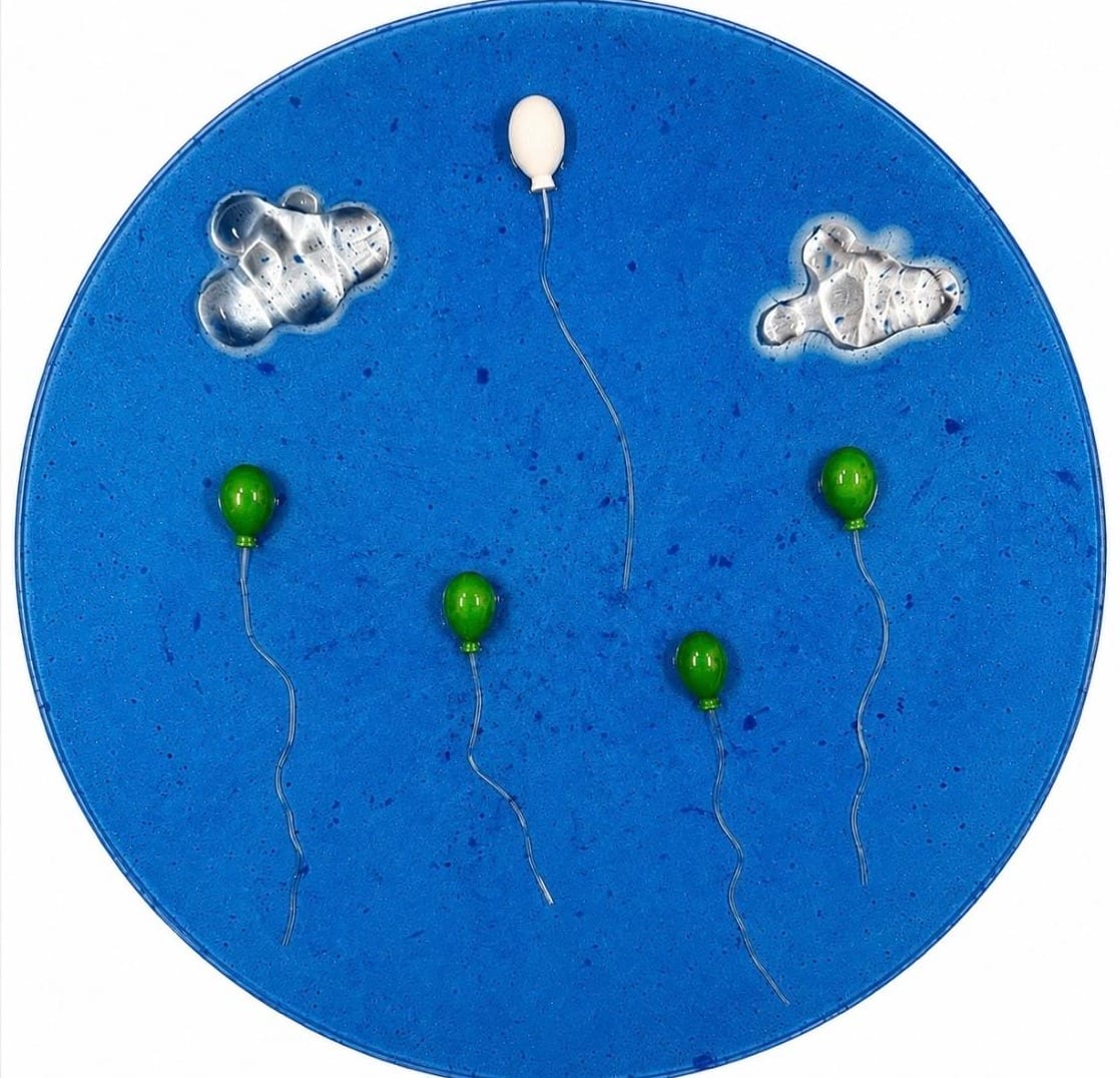 Round blue panel with four green balloons, one white balloon and two silver clouds
